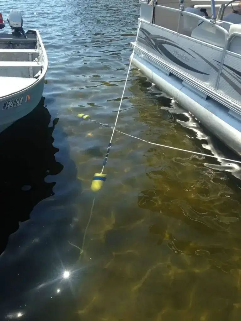 A noodle float is submerged and tied between two boats floating on clear water near Great Northern Docks, sunlight reflecting on the surface.