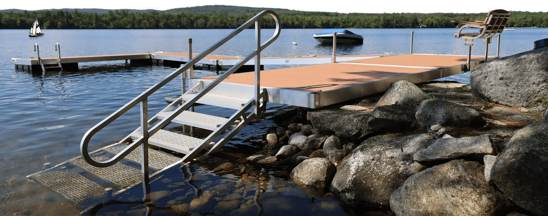 A metal dock by Great Northern Docks with stairs extends into a calm lake surrounded by rocks, boats, and forested hills in the background.