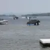 Several boats float on a lake near Maine Docks under a clear sky, secured by Mooring Ball, with wooded hills in the background.
