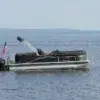 A pontoon boat with a U.S. flag is anchored to a Mooring Ball near Great Northern Docks, with calm water and distant land under a clear sky.