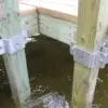 Close-up of two 4x4 Post Brackets securing wooden dock posts to a timber dock, partially submerged in water.