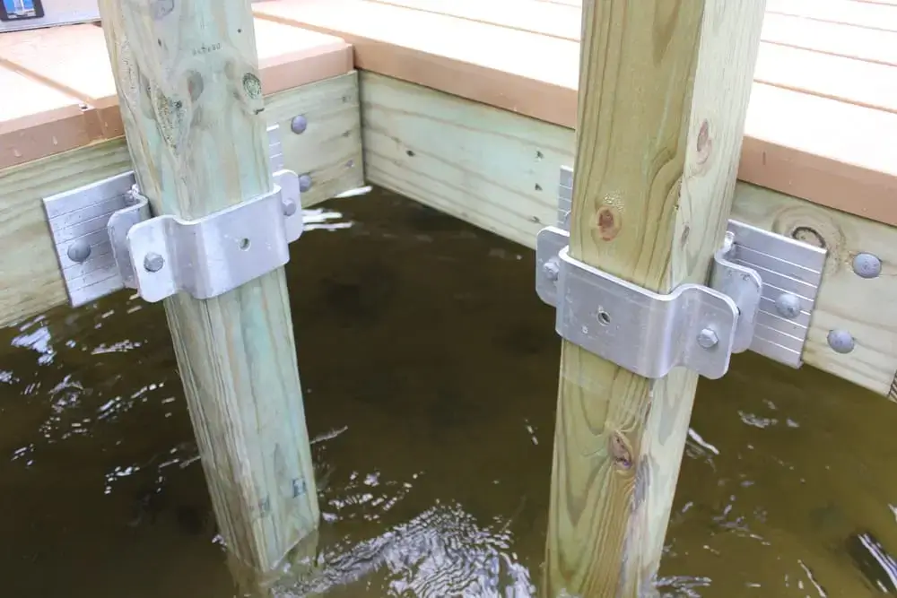 Close-up of two 4x4 Post Brackets securing wooden dock posts to a timber dock, partially submerged in water.
