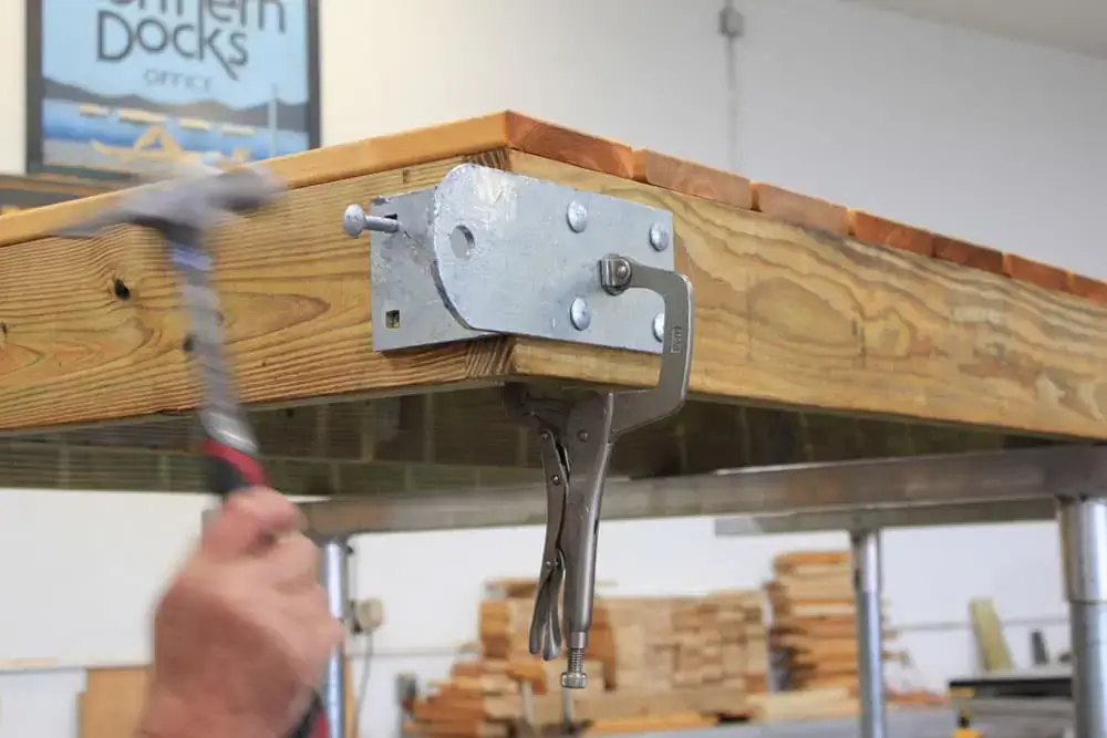 A person uses a hammer on a Reinforced Hinge Plate attached to wood, stabilized by locking pliers—a technique common at Maine docks by Great Northern Docks.