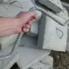 A hand holds a DIY Anchor Rod for Concrete Block in front of broken slabs with metal handles, commonly used near Maine Docks or beside wood docks.