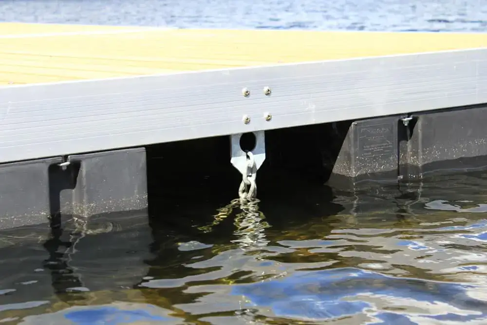 Close-up of an Anchor Plate Keyhole from Great Northern Docks attached under a floating dock frame, with metal chain and water reflections visible.