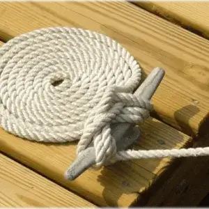 A coiled white rope is neatly placed on a wood dock, with one end tied to a Dock Cleats Galvanized (2 Pack) gray cleat.
