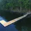 A Floating Dock from Great Northern Docks extends over calm, dark water near a forested shoreline, with boats visible in the distance.