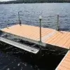 A dock with 1.5" Sch. 40 Galvanized Pipe railings and lights extends over a lake, with grated platform sides and Maine Docks along the tree-lined shore.