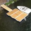 An Aluminum Ladder for Dura-LITE Docks is attached to a floating dock on a lake, with green trees and rocks along the shore at Great Northern Docks.