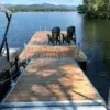A wooden dock by Great Northern Docks on a lake with two Adirondack chairs, overlooking trees and mountains in the background.