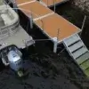 A pontoon boat is docked beside a wooden dock from Great Northern Docks, with a metal ramp using 1.5" Sch. 40 Galvanized Pipe leading into the water over rocks.