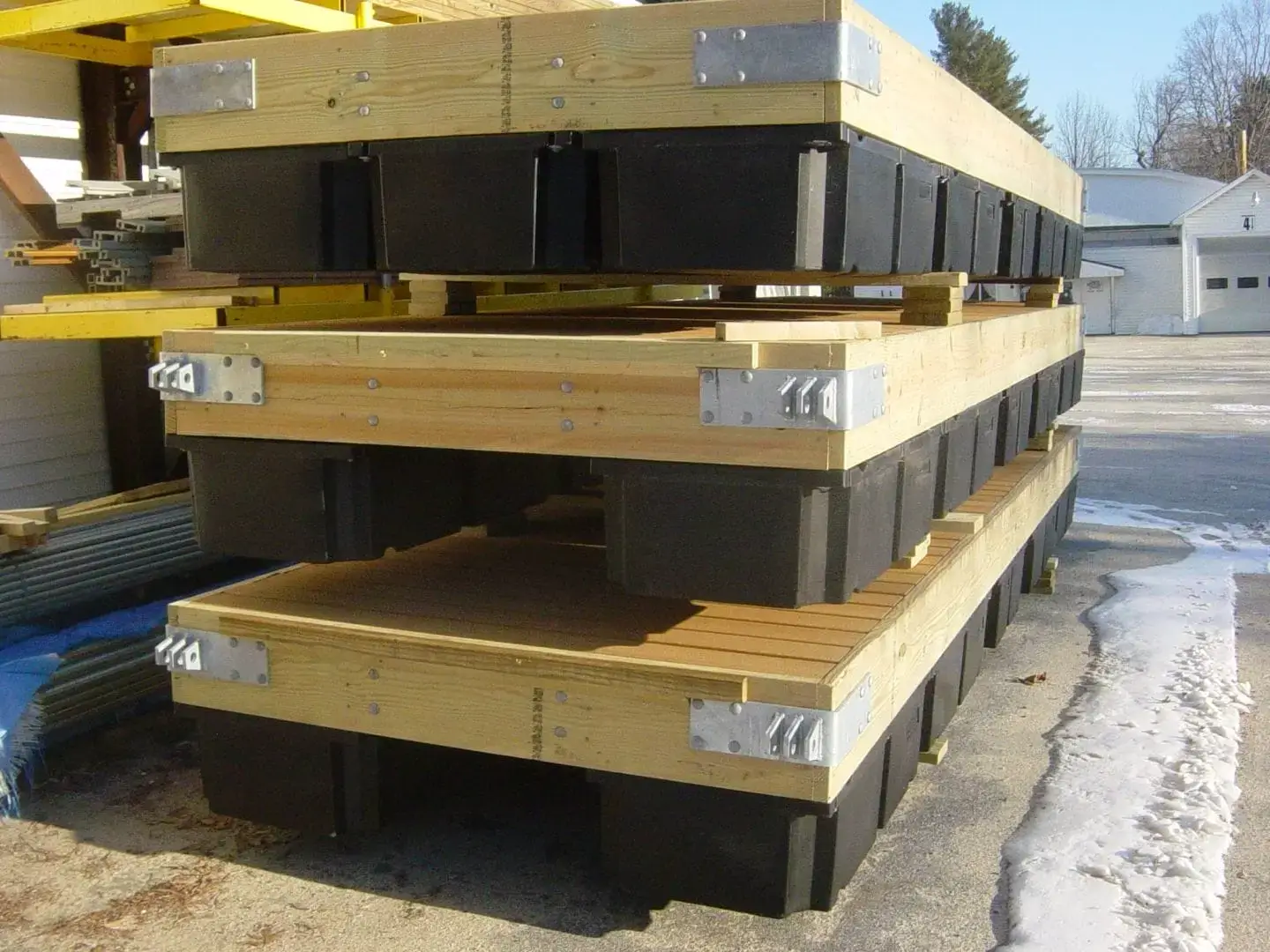 Three Dock Float Attachment Kit (Foam Filled) units from Great Northern Docks with wood frames and black floats, stacked outdoors on pavement near a building.