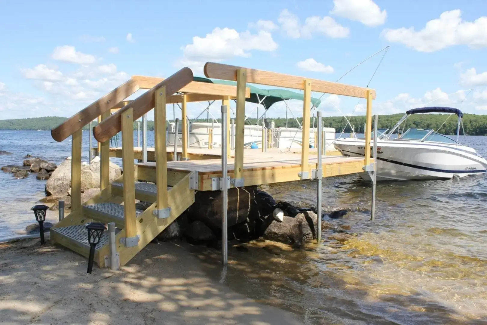 A dock built with 1.5" Sch. 40 Galvanized Pipe extends from the sandy shore into clear lake water, classic Maine Docks style by Great Northern Docks.