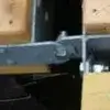 Close-up of a Reinforced T-Hinge Plate attached with bolts and screws to wooden beams, connecting two pieces of wood in sturdy Maine Docks.