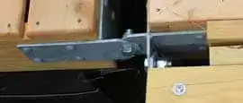 Close-up of a Reinforced T-Hinge Plate attached with bolts and screws to wooden beams, connecting two pieces of wood in sturdy Maine Docks.