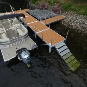 A Fixed Dock on Legs is docked at a wooden pier with a metal gangway; chairs and flowers line the shore beside it.