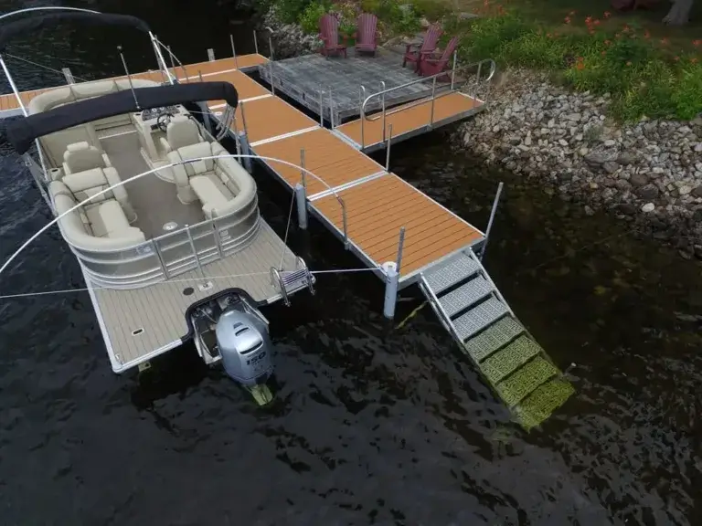 A Fixed Dock on Legs is docked at a wooden pier with a metal gangway; chairs and flowers line the shore beside it.