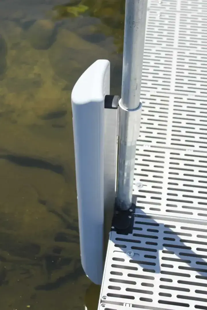 The Guardian Bumper with Pipe Bracket is a white dock bumper mounted on a metal dock in clear water, perfect for Maine docks with visible underwater rocks or plants.