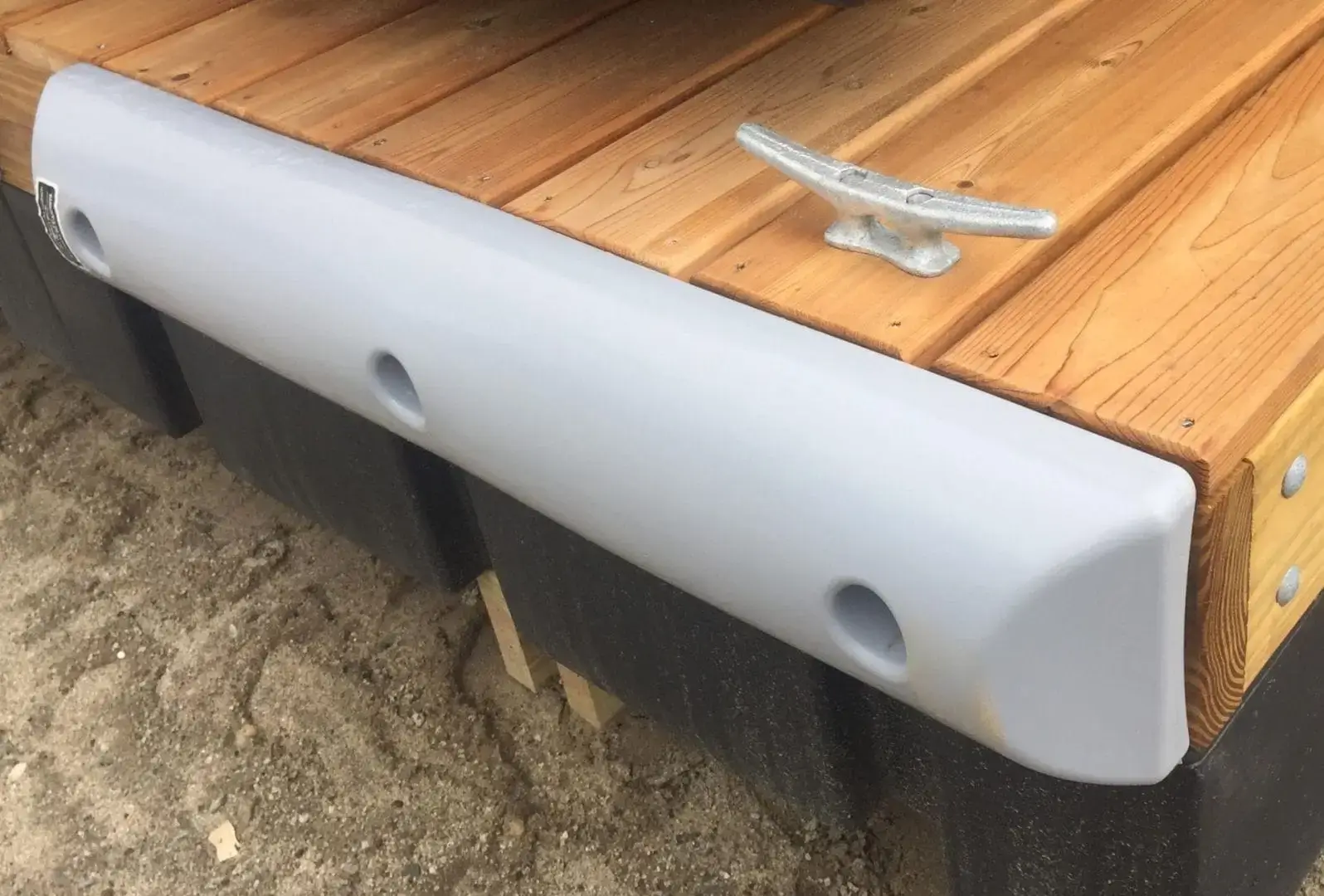 The Guardian Bumper, in gray, attaches to the edge of a wood dock with a metal cleat—ideal for Maine docks with sand below.