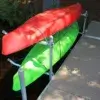 A red and a green kayak rest on a Kayak & Canoe Arm (Single Arm) rack by Great Northern Docks, attached to a wood dock by the tree-lined water.
