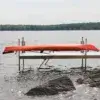 A Kayak & Canoe Arm (Single Arm) secures a red kayak upside down on a wooden dock over a calm lake, framed by rocks and distant tree-lined shores—classic Great Northern Docks.