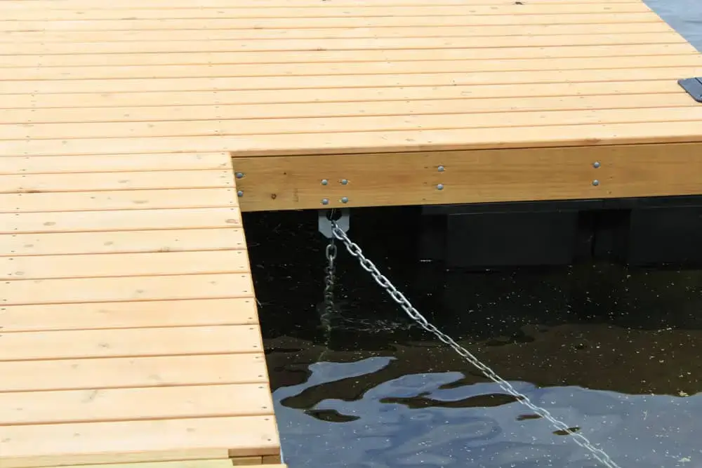 Close-up of an Anchor Plate Keyhole by Great Northern Docks, with metal chains securing it to black floats as sunlight reflects on the water below.