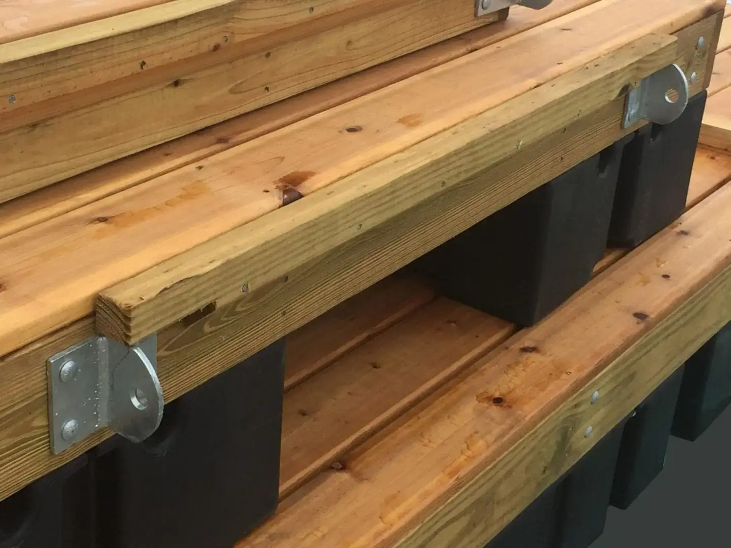 Close-up of stacked wood docks with metal brackets, supported on black plastic floats—featuring the T-Hinge Plate.