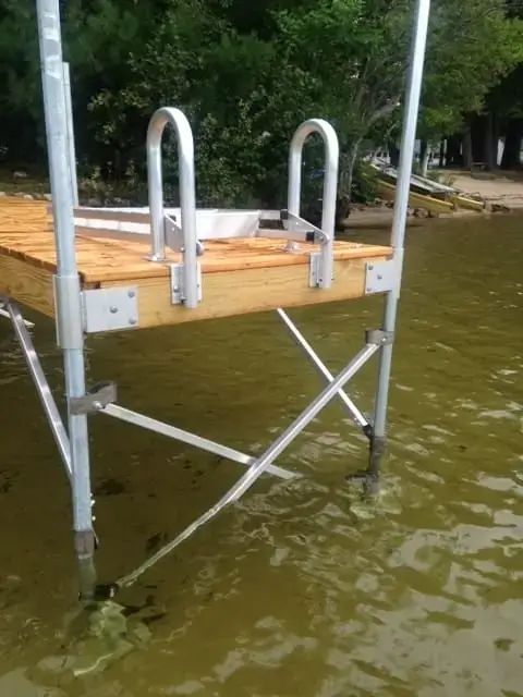 An Aluminum Dock Ladder from Great Northern Docks stands in shallow, clear water by a shoreline with trees in the background.