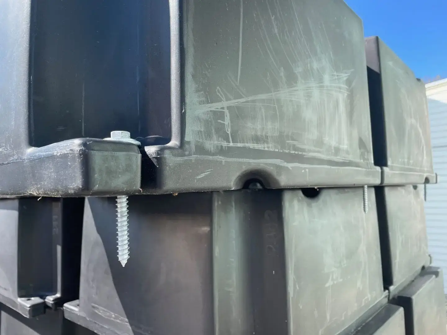 Close-up of Dock Float Attachment Kit (Foam Filled) with stacked black containers and a silver screw, outdoors under a blue sky at Great Northern Docks.