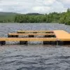 An Anchor Plate Keyhole by Great Northern Docks is installed on a wooden dock extending into a lake, surrounded by trees and hills under a partly cloudy sky.