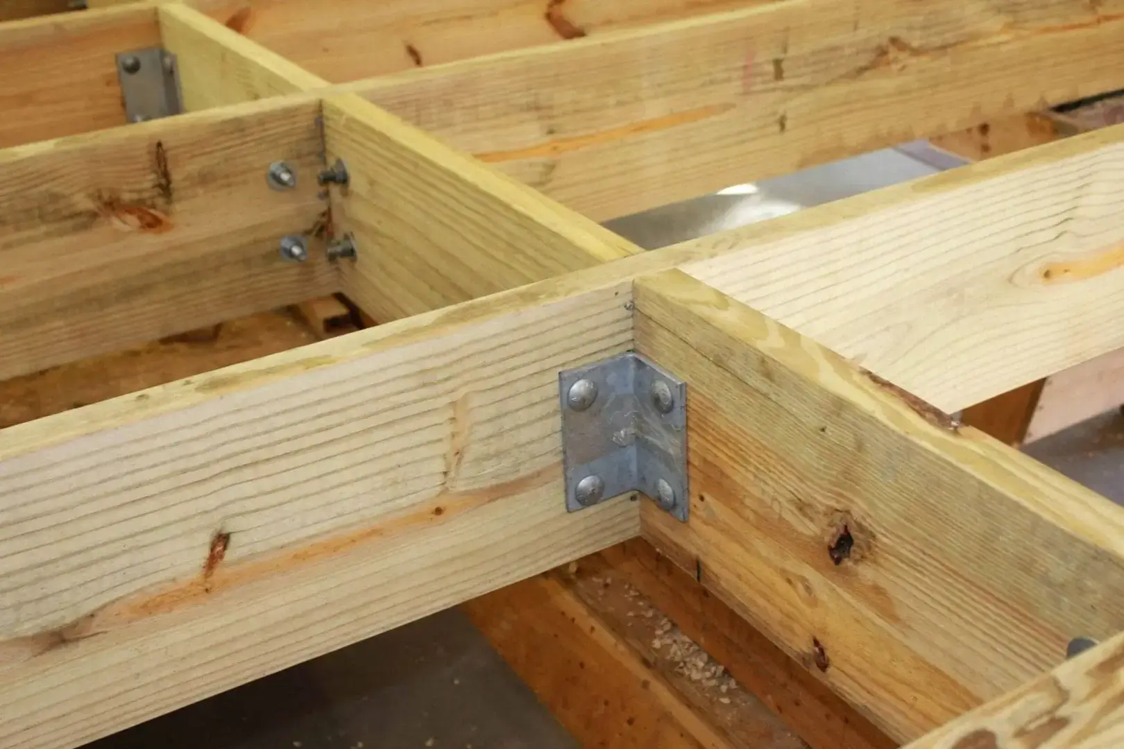 Close-up of intersecting wooden beams joined with a Corner Iron 90º bracket and bolts, like those used in Maine docks by Great Northern Docks.