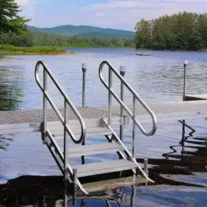 A Fixed Dock on Legs with stairs extends into a peaceful lake bordered by trees and hills beneath a partly cloudy sky.