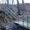 A rail bracket supports a staircase and bridge ascending a leaf-strewn forested hill, surrounded by tall trees, reminiscent of classic Wood Docks.