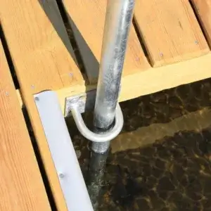 Close-up of a Maine dock with a metal pole secured in place over clear, shallow water. Sunlight highlights the wood planks and casts shadows on the water below.