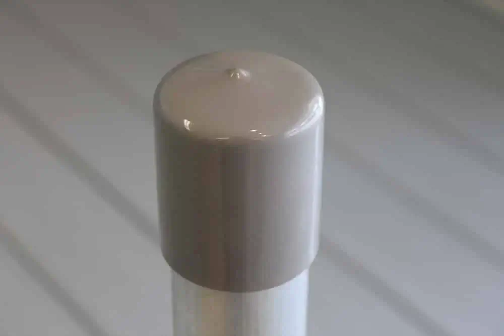 A close-up of a beige Pipe Safety Cap (6 Pack) from Great Northern Docks on a metal post, set against a blurred striped background.