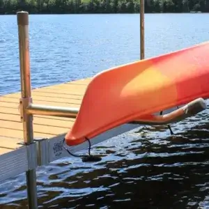 A red and orange kayak sits on a Kayak & Canoe Arm (Single Arm) by Great Northern Docks, mounted to a wooden dock by a calm lake with trees in the background.
