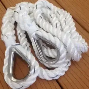 A coiled white braided rope with metal thimbles at each end, ideal for securing boats to Maine Docks, rests on a brown wooden surface.