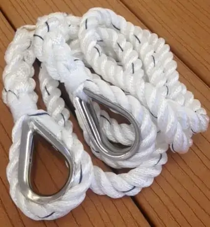 A coiled white braided rope with metal thimbles at each end, ideal for securing boats to Maine Docks, rests on a brown wooden surface.