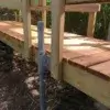 A close-up of a wooden footbridge with sturdy railings and a 1.5" Sch. 40 Galvanized Pipe support post by Great Northern Docks, surrounded by lush greenery.