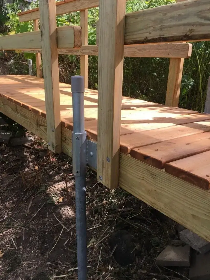 A close-up of a wooden footbridge with sturdy railings and a 1.5" Sch. 40 Galvanized Pipe support post by Great Northern Docks, surrounded by lush greenery.