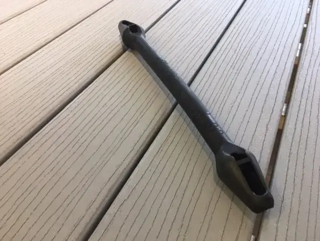 A black Mooring Snubber with a handle and two rectangular openings lies diagonally on light gray composite deck boards from Great Northern Docks.
