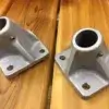 Two Mooring Whip (2 Pack) brackets with angled cone-shaped mounts and four screw holes each, great for securing wood or aluminum docks, shown on a wooden surface.