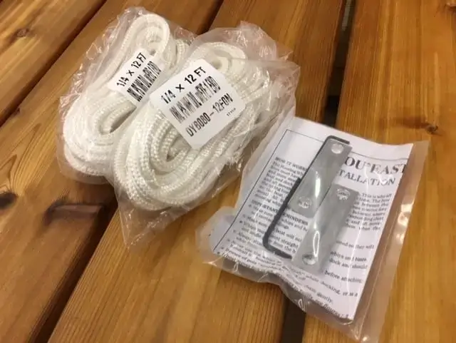 Two coiled Mooring Whip (2 Pack) ropes, a metal bracket, and an instruction sheet are displayed on wood. Ropes are labeled 1/4 x 12 FT.