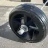 Close-up of a large black plastic wheel with grooved tread, attached to a metal axle on a concrete surface—ideal for use with Maine Docks or Aluminum Docks.