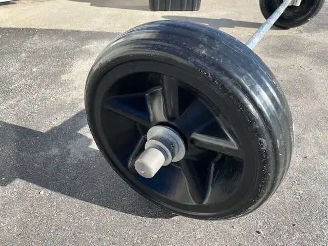 Close-up of a large black plastic wheel with grooved tread, attached to a metal axle on a concrete surface—ideal for use with Maine Docks or Aluminum Docks.