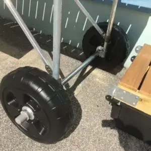 Close-up of large black wheels on a metal frame next to a wooden bench, part of Dock Wheel Kits by Great Northern Docks on a sunny outdoor surface.