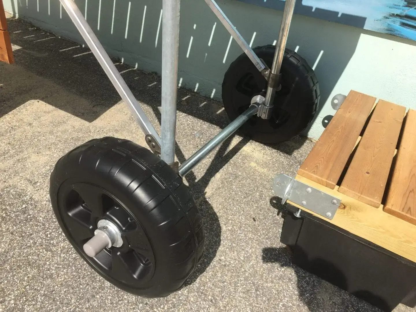 Close-up of large black wheels on a metal frame next to a wooden bench, part of Dock Wheel Kits by Great Northern Docks on a sunny outdoor surface.