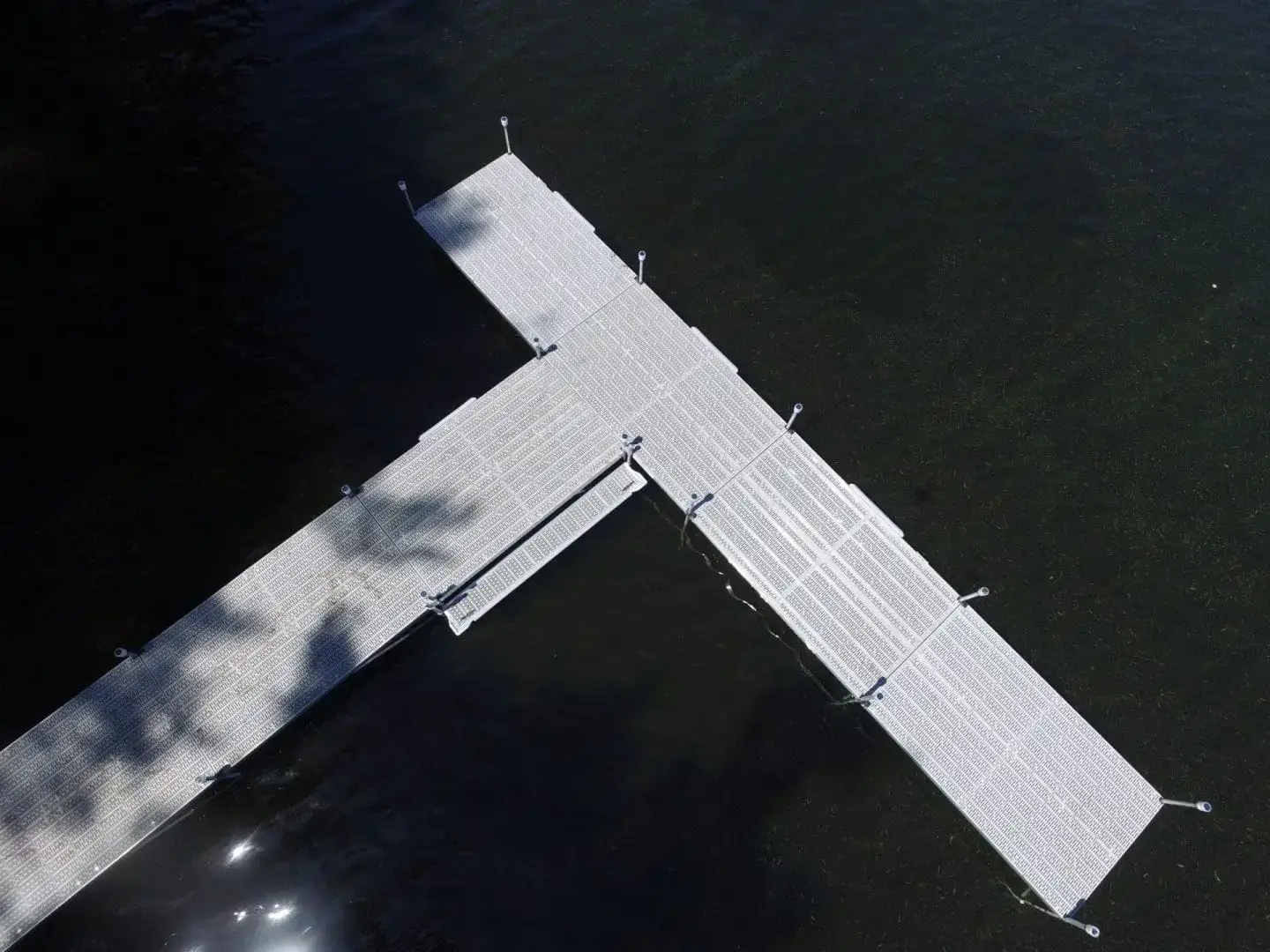Aerial view of Boarding Steps from Great Northern Docks, a T-shaped aluminum dock over dark water with sunlight and tree shadows on the surface.