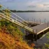 A wooden dock by Great Northern Docks with sturdy railings extends from a grassy shore into a calm lake, framed by trees and a partly cloudy sunset sky.