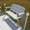 A Bench with armrests and cup holders is installed on a Great Northern Docks wood dock above shallow water near trees.